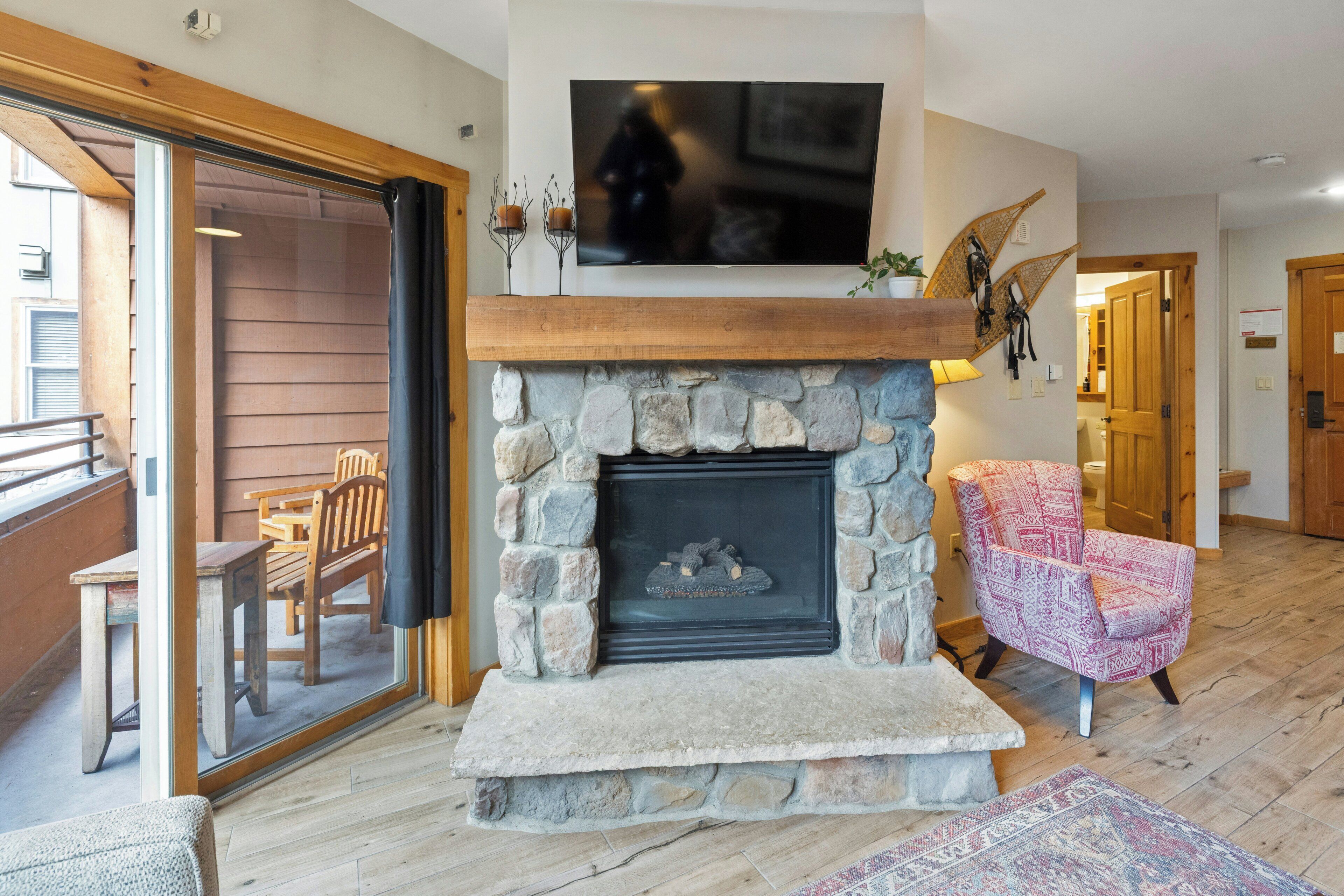 A stone fireplace with a TV above it, a wooden chair, and a patterned rug.