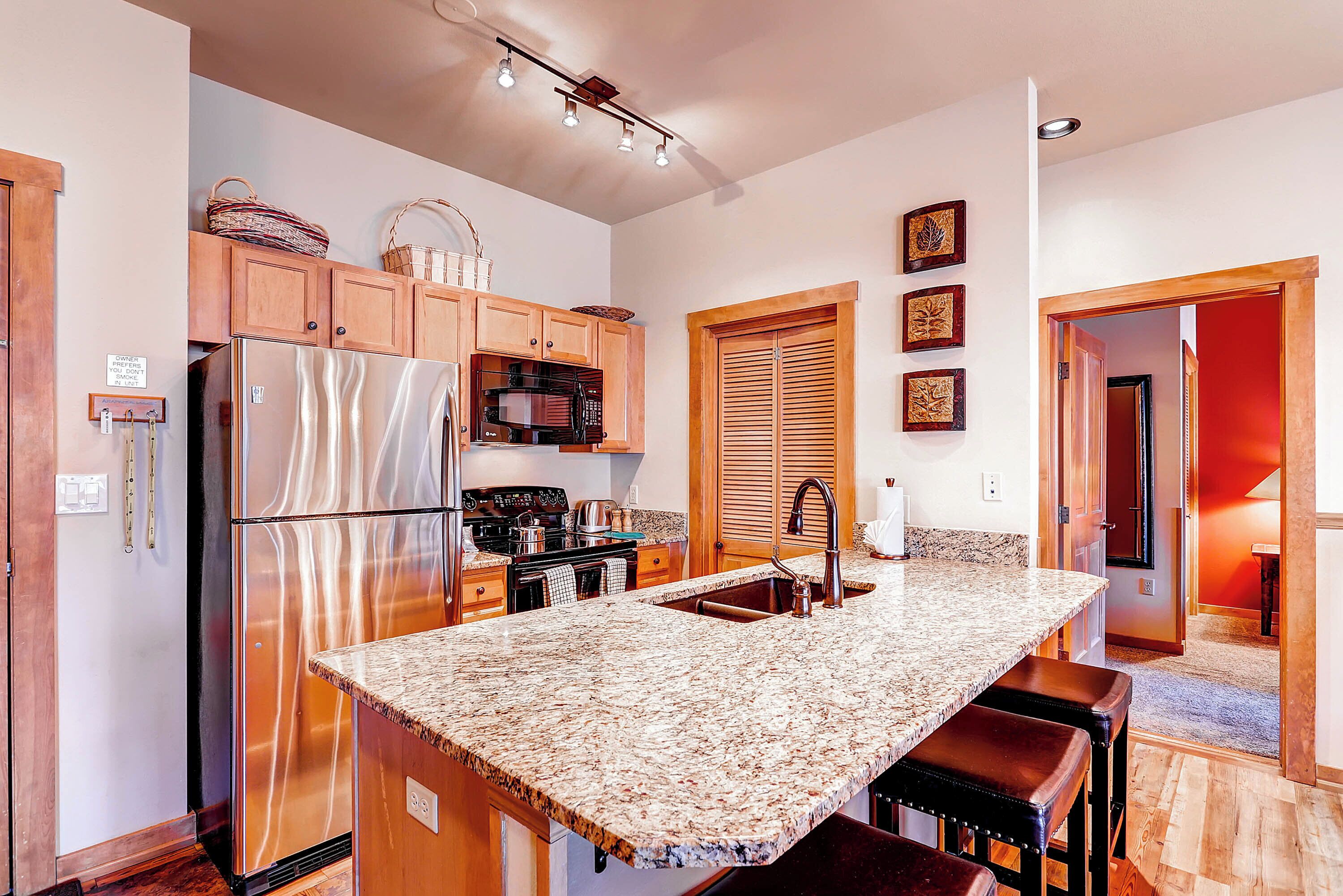 A modern kitchen with stainless steel appliances, a granite countertop, wooden cabinets, and a built-in oven.