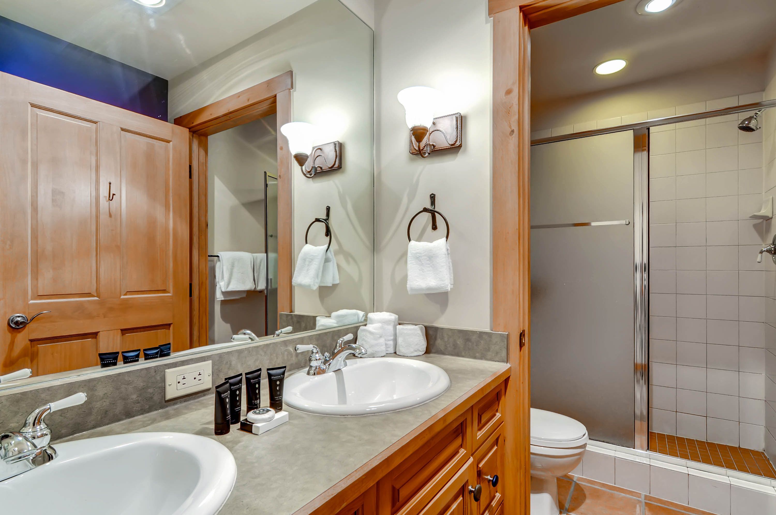 A bathroom with two sinks, a mirror, a shower, and wooden cabinets.