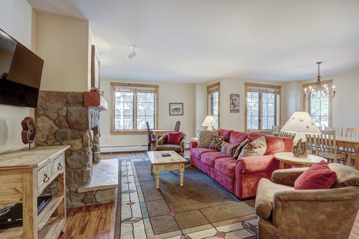 A living room with a stone fireplace, a red sofa, a wooden coffee table, and a TV mounted on the wall.