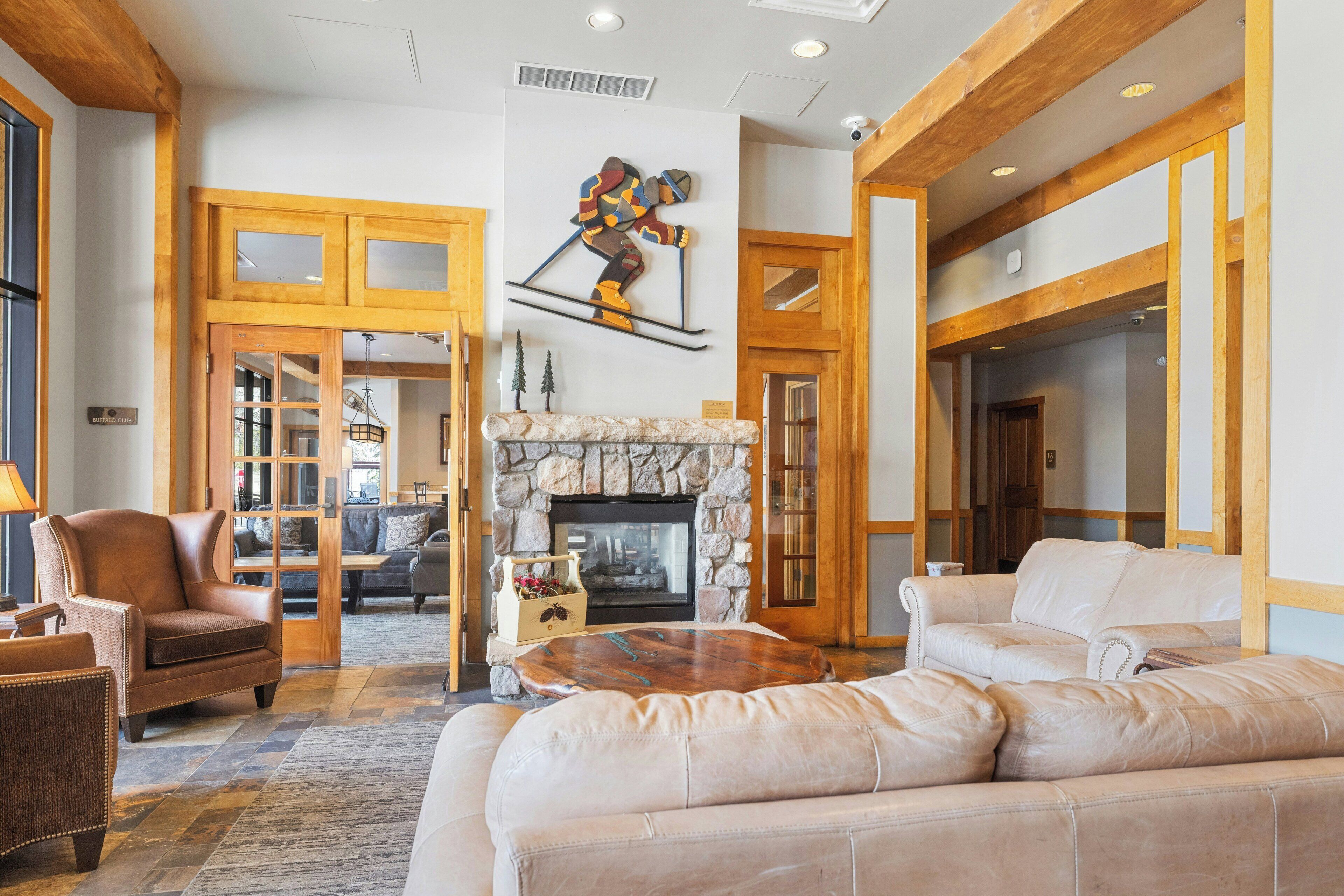 Ein geräumiges Wohnzimmer mit Kamin aus Stein, Ledersofas und Kunstwerken zum Thema Skifahren.