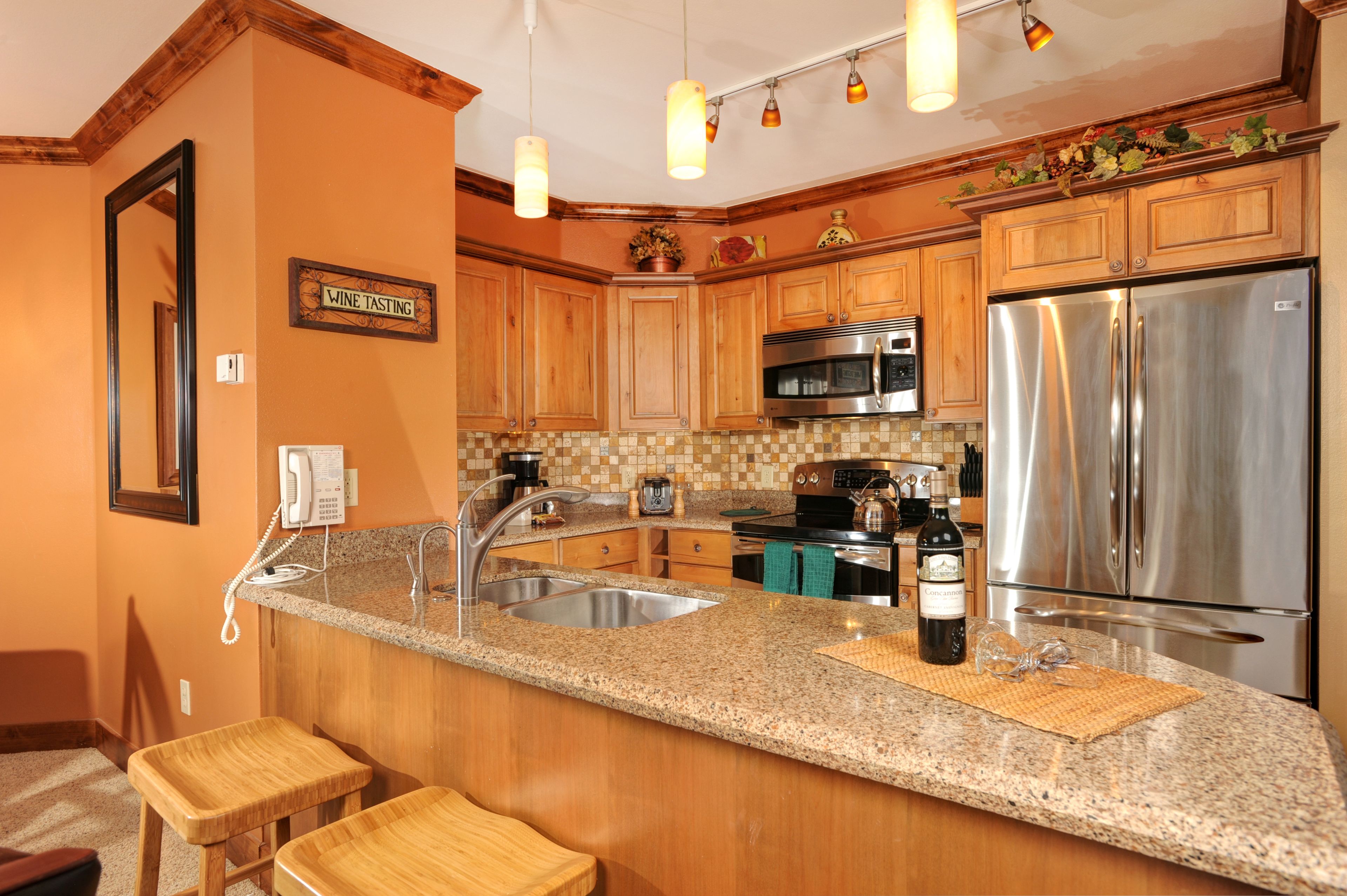 Cocina con armarios de madera, encimeras de granito y electrodomésticos de acero inoxidable, además de un letrero que anuncia degustación de vinos.