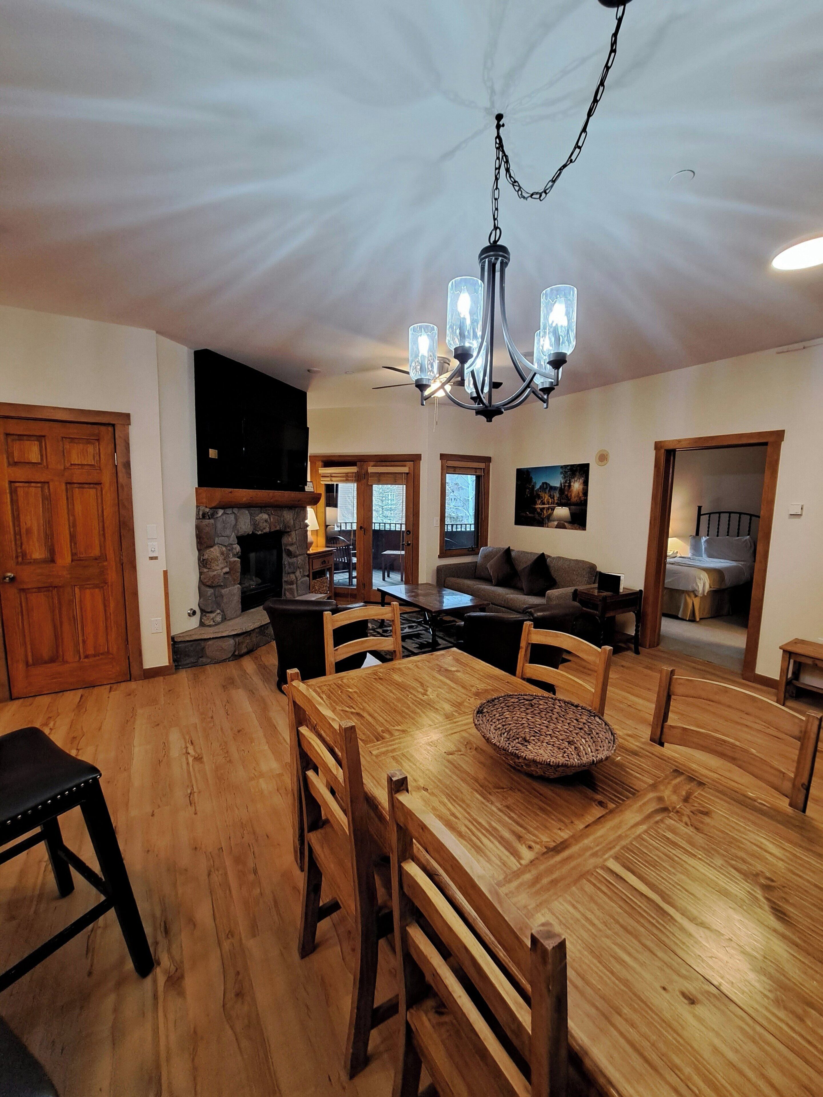 Un vaste espace de vie comprenant une table à manger en bois, des chaises, une cheminée et un coin salon confortable avec un canapé et des fauteuils.