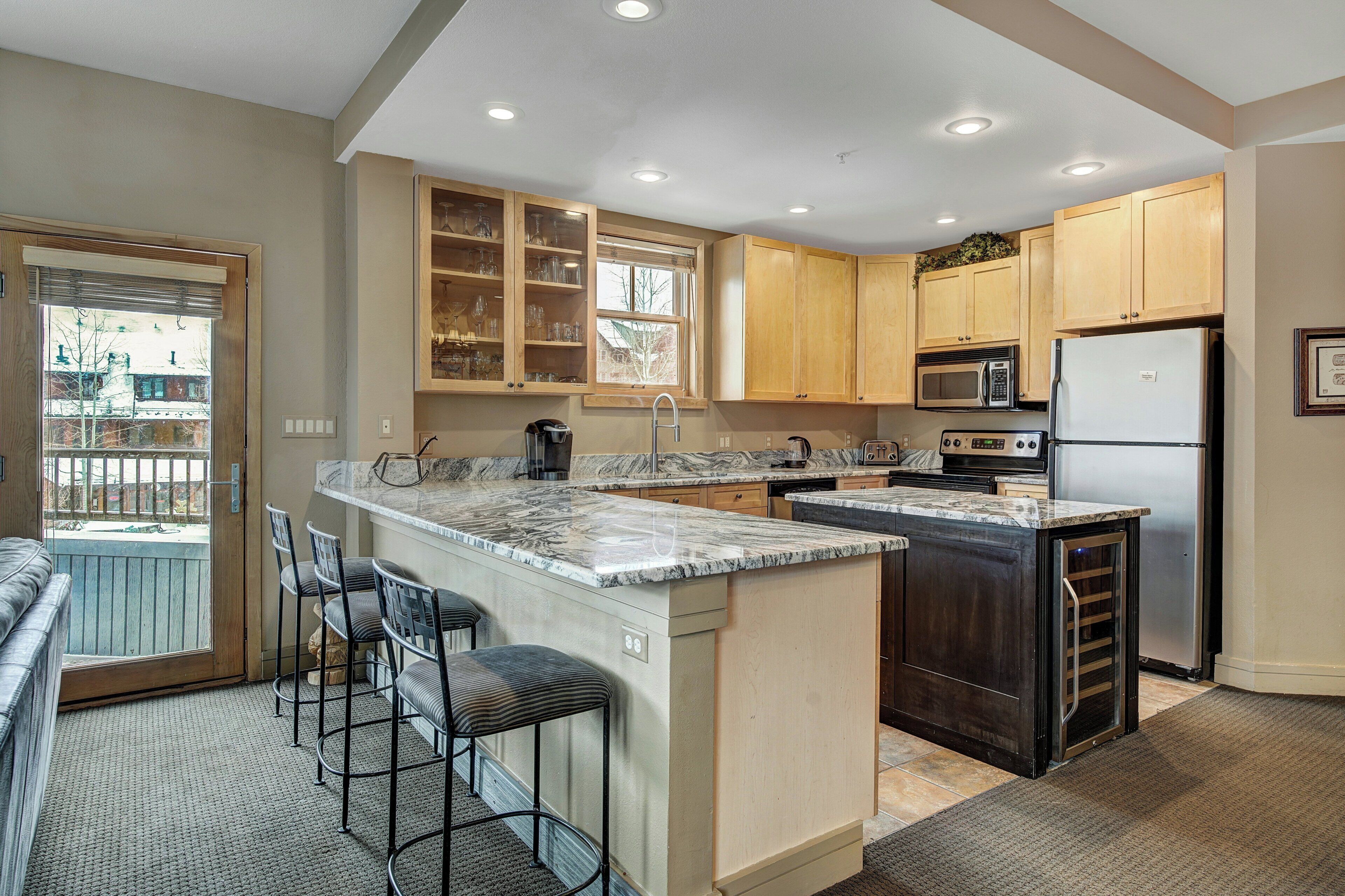 A modern kitchen with a large island, bar stools, wooden cabinets, and a built-in microwave.