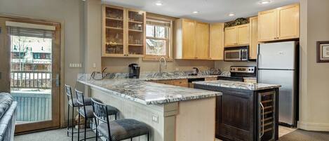 A modern kitchen with a large island, bar stools, wooden cabinets, and a built-in microwave.
