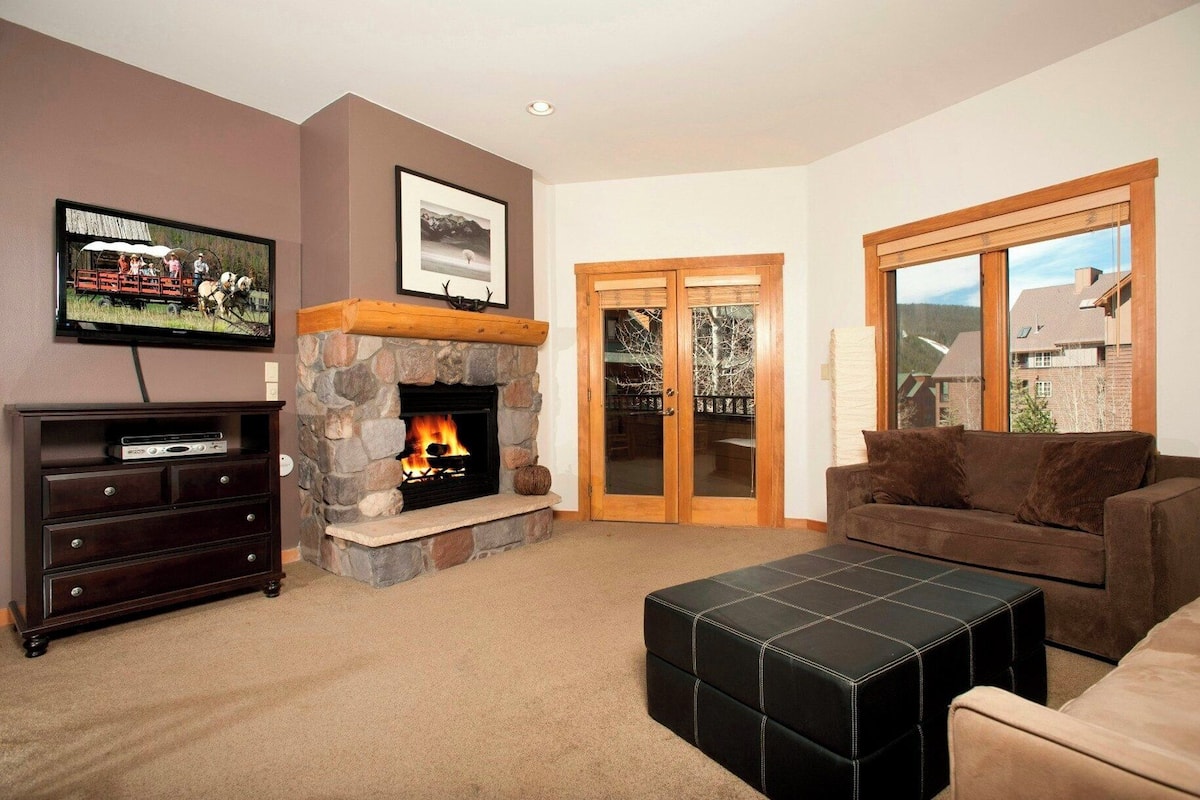 A living room with a stone fireplace, a television, a sofa, and a large window.