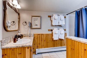 A bathroom with a wooden vanity, a large mirror, a framed picture, and multiple towels hanging on a rack.