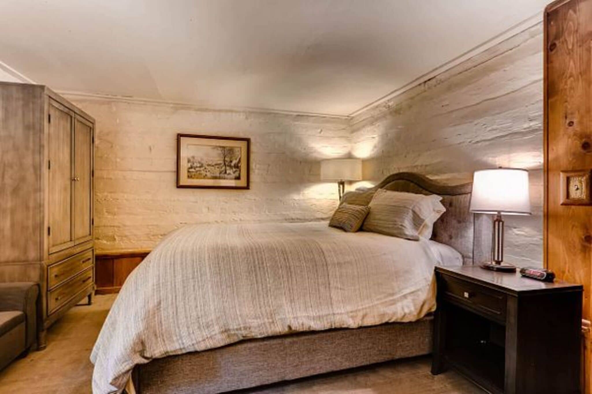 A bedroom with a bed, wooden wardrobe, nightstands, and a framed picture on the wall.