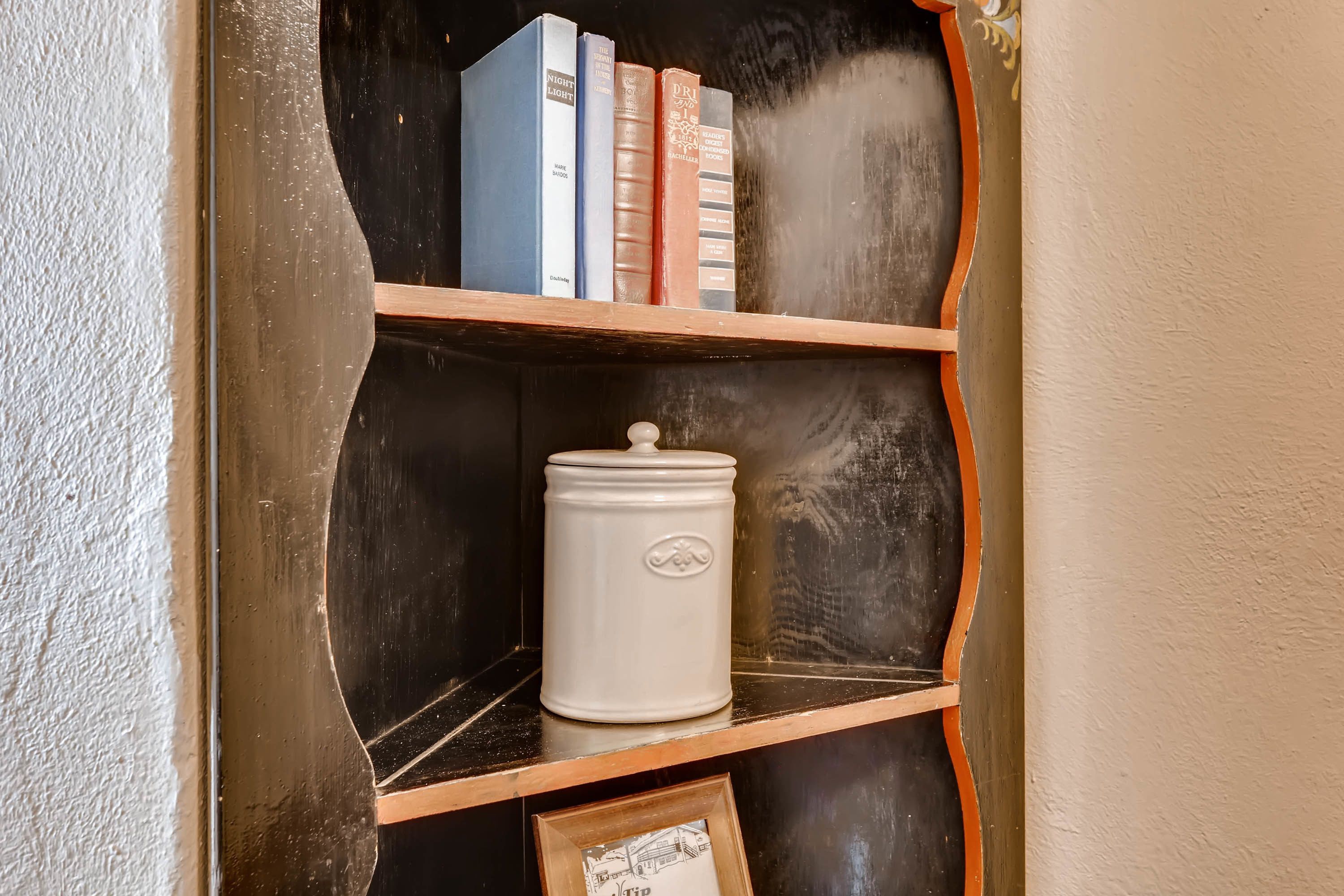 A bookshelf with books and a white ceramic container.