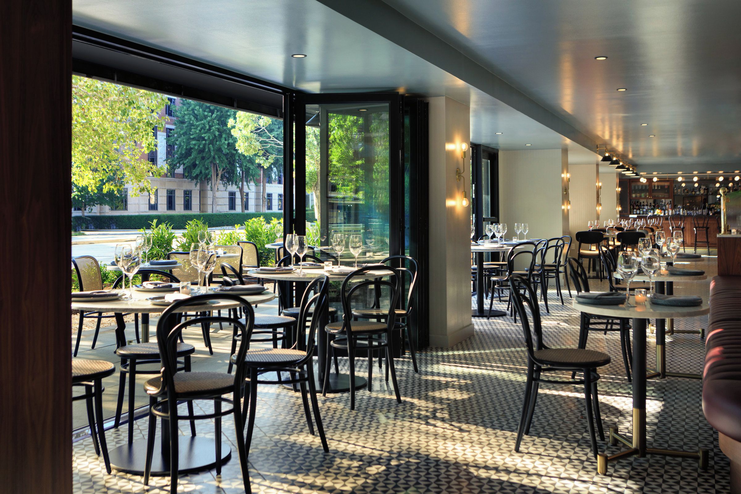 An indoor dining area with tables and chairs, large windows, and a view of the street outside.