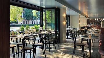 An indoor dining area with tables and chairs, large windows, and a view of the street outside.