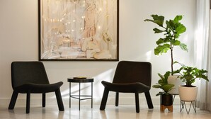 A modern room with two dark chairs, a small round table, a large abstract painting, and a potted plant. - Kimpton Banneker Hotel by IHG (Washington)