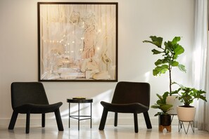 Une pièce moderne avec deux fauteuils sombres, une petite table ronde, une grande peinture abstraite et une plante en pot.