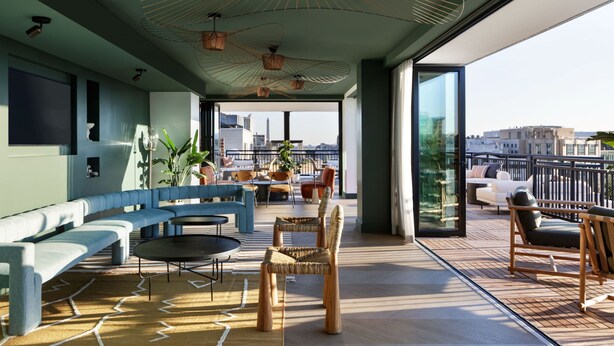 A modern lounge area with a curved blue sofa, a round table, and wicker chairs. - Kimpton Banneker Hotel by IHG (Washington)