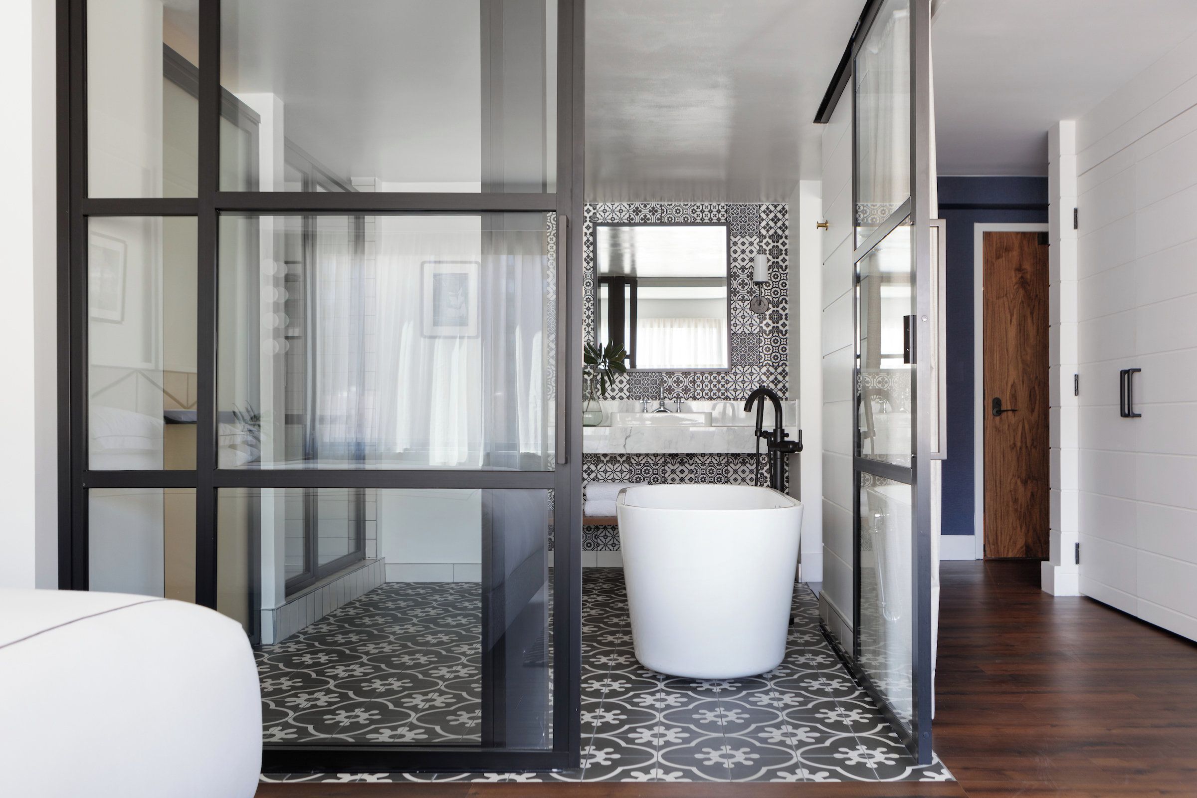 A modern bathroom with a glass shower enclosure, a white sink, and patterned floor tiles.