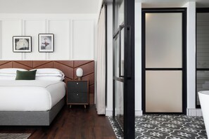 A hotel room with a bed, a nightstand, a mirror, and a door leading to another room. - Kimpton Banneker Hotel by IHG (Washington)