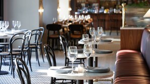 A restaurant interior with round tables, chairs, and a bar area in the background. - Kimpton Banneker Hotel by IHG (Washington)