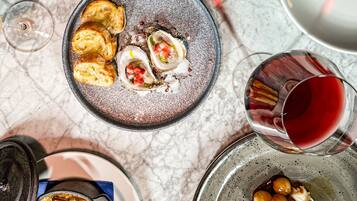 A table with various dishes, including bread, oysters, and a pot of food, along with glasses of red wine.
