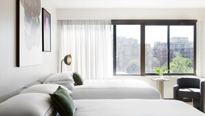 A hotel room with two beds, a desk, and a chair. There is a large window with a view of buildings and trees. - Kimpton Banneker Hotel by IHG (Washington)