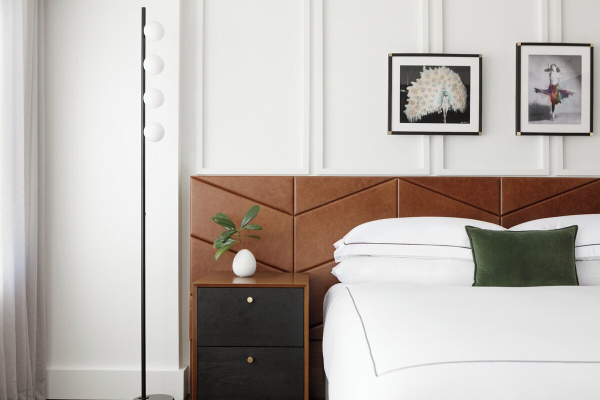 A neatly arranged hotel room with a bed, a nightstand with a plant, and two framed pictures on the wall.