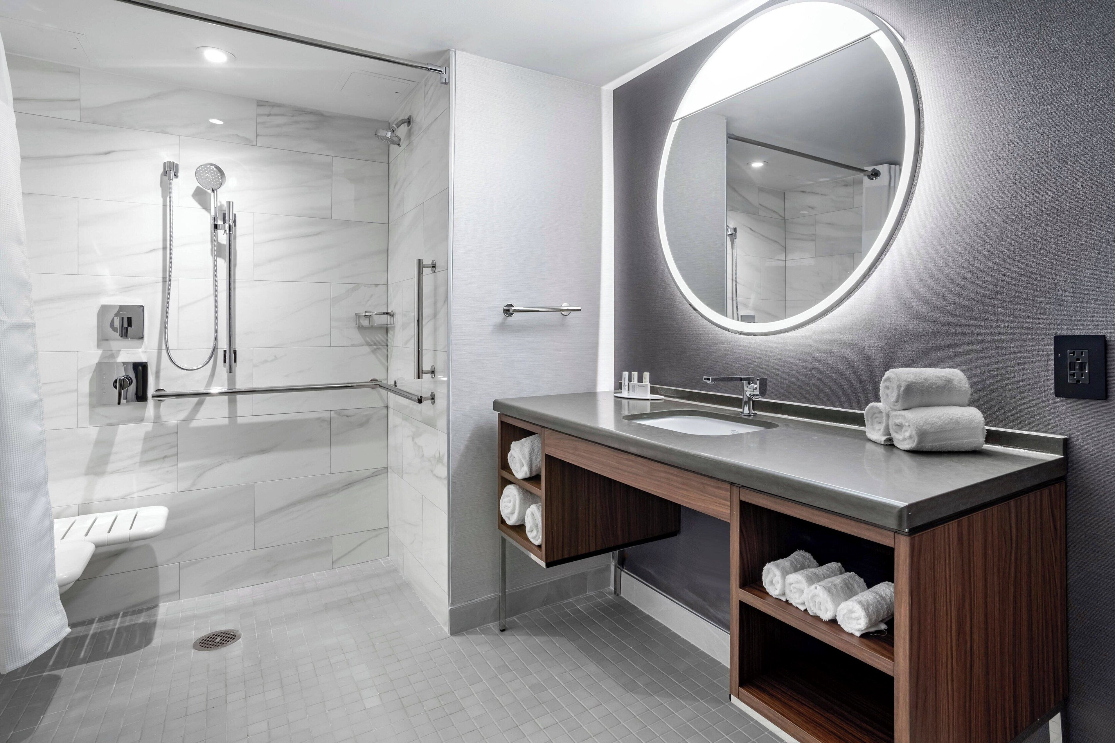 Une salle de bain moderne dotée d’une douche à parois de verre, d’un meuble-lavabo avec un grand miroir et de porte-serviettes intégrés.