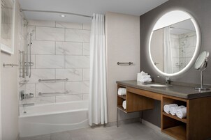 A modern bathroom with a bathtub, shower, vanity with a mirror, and towel storage.