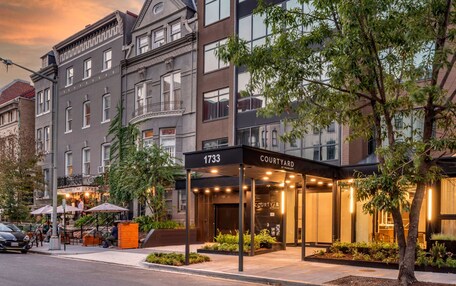 A hotel entrance with a covered outdoor seating area, a sign reading "COURTYARD BY PERAVENT," and a classic building facade in the background.