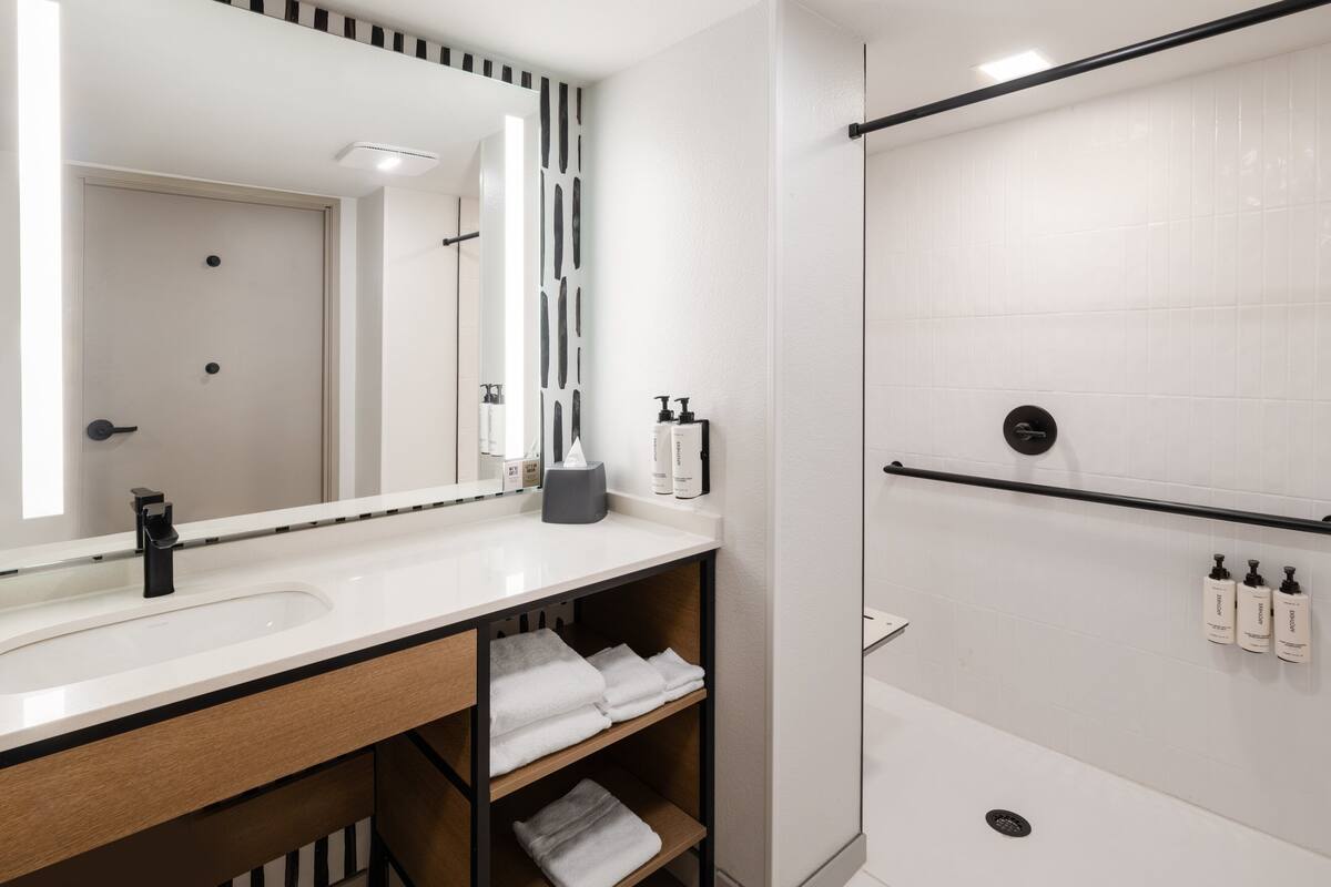 A modern bathroom with a large mirror, white tiles, a black towel rack, and a shower area.