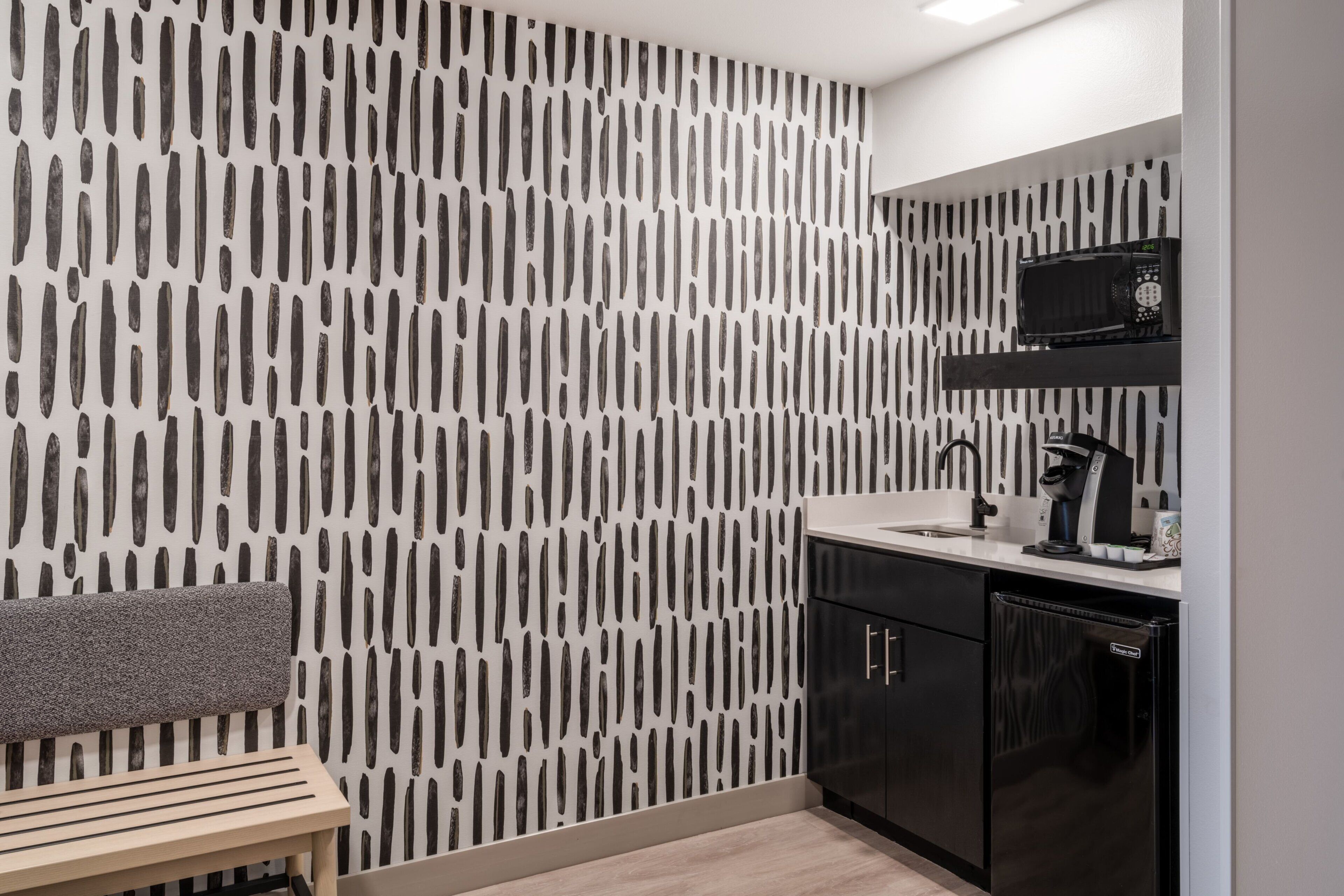 A modern kitchen with a patterned wall, a microwave, a coffee machine, and black cabinets.