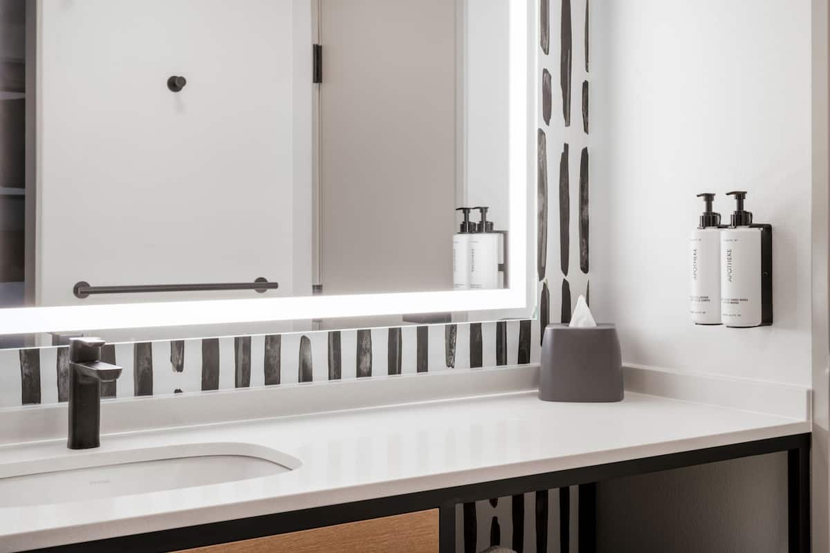 A modern bathroom with a white sink, a large mirror, and two toiletry bottles on the wall.