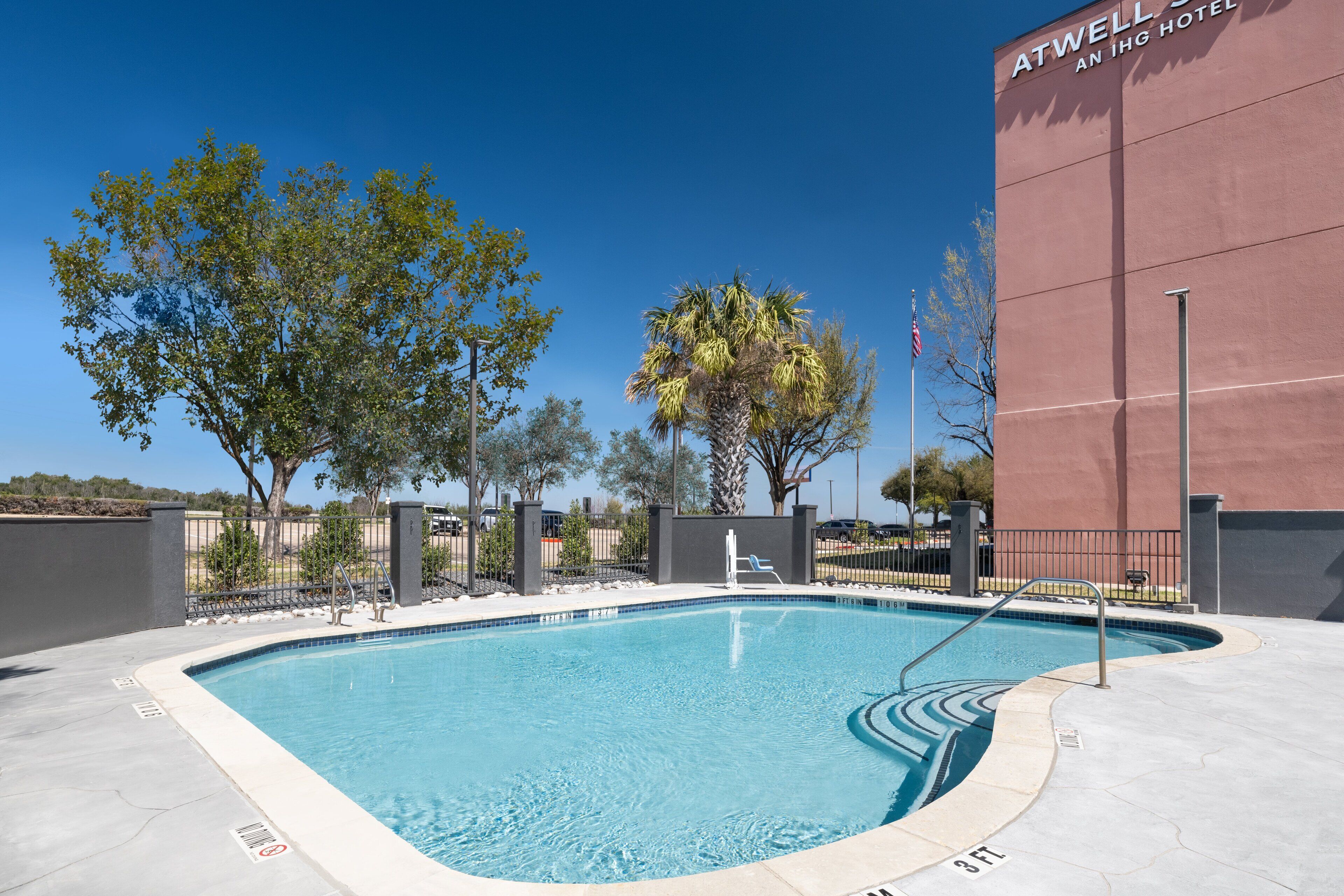 Una piscina con indicador de profundidad de 3 pies, rodeada por un deck de concreto, árboles y un edificio con el letrero 'ATWELL HOTEL'.