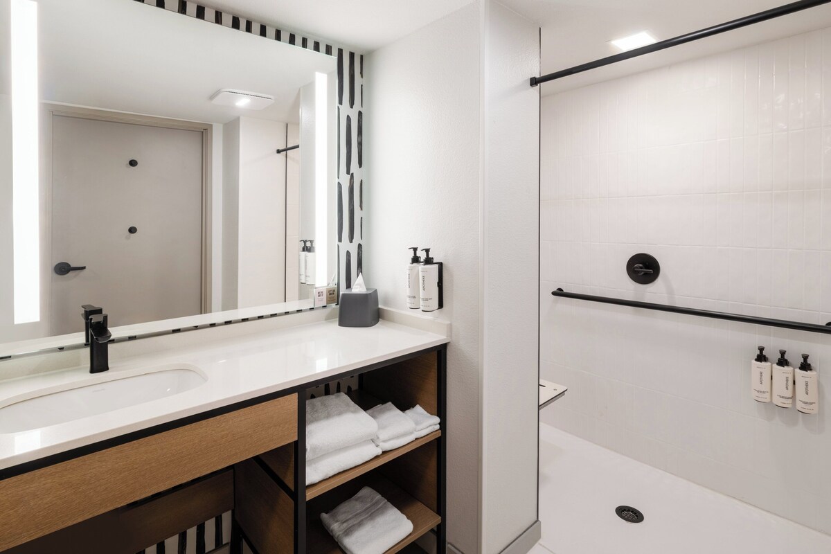 A modern bathroom with a large mirror, white tiles, a black towel rack, and a shower area.