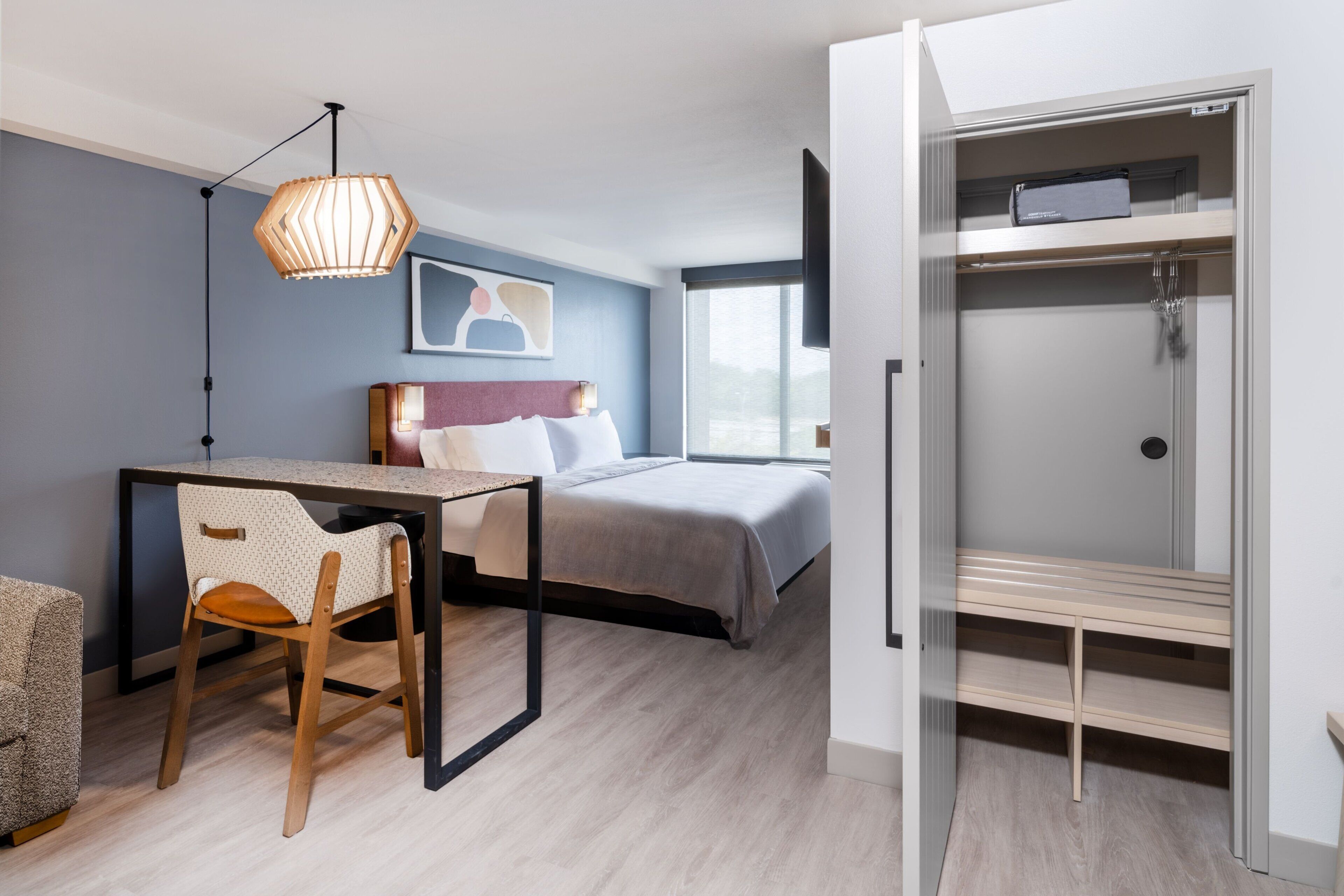Ett modernt hotellrum med en säng, ett skrivbord, en stol och en rymlig klädkammare.