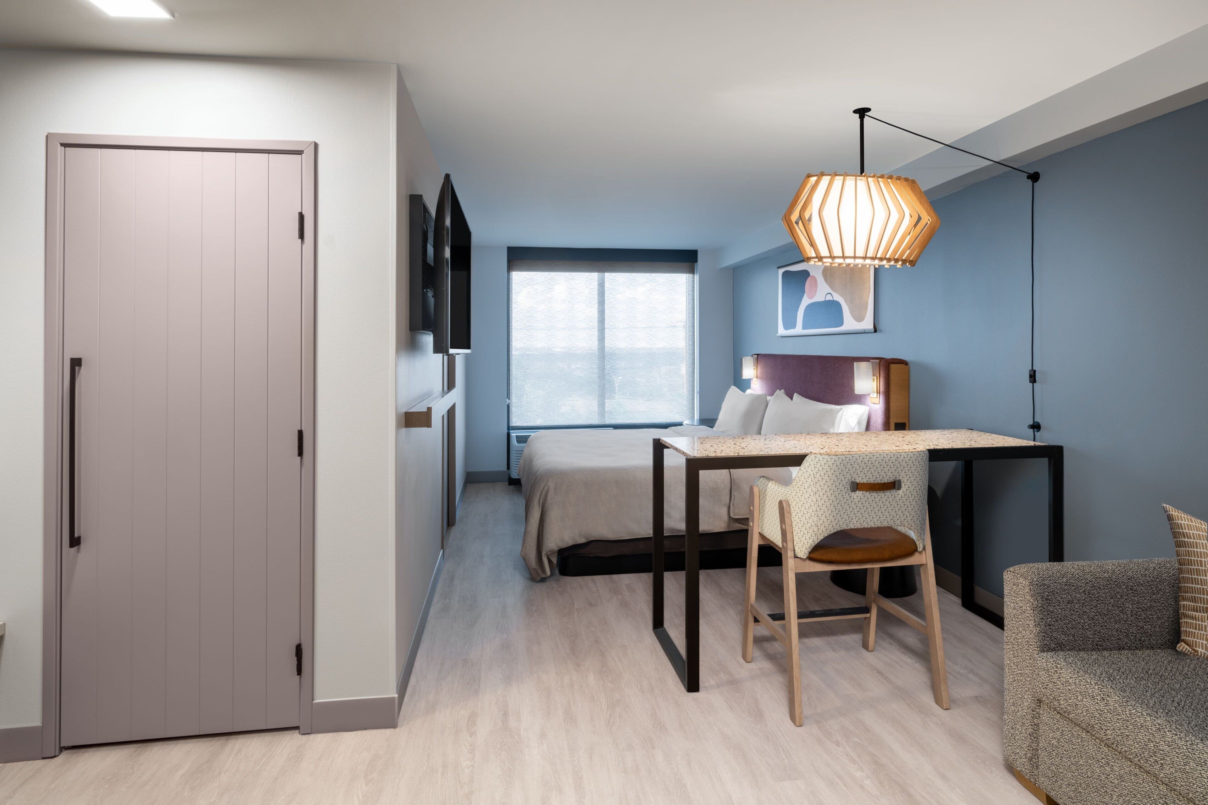 Une chambre de taille modeste, comprenant un lit, un bureau avec une chaise, une télévision et une armoire.