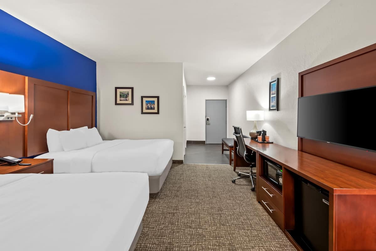 A hotel room with two beds, a desk with a computer, a TV, and a minibar.