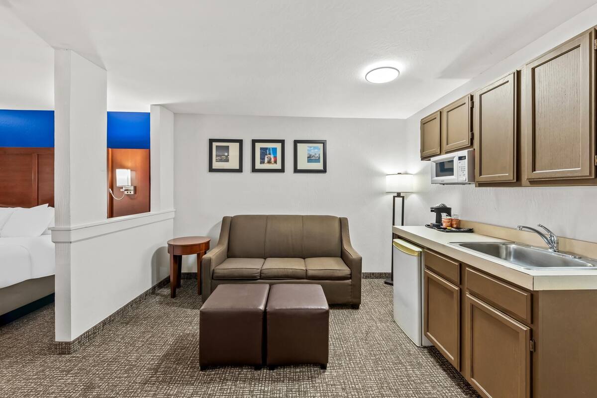 A compact hotel room with a kitchenette, a sofa, a small table, and a bed.