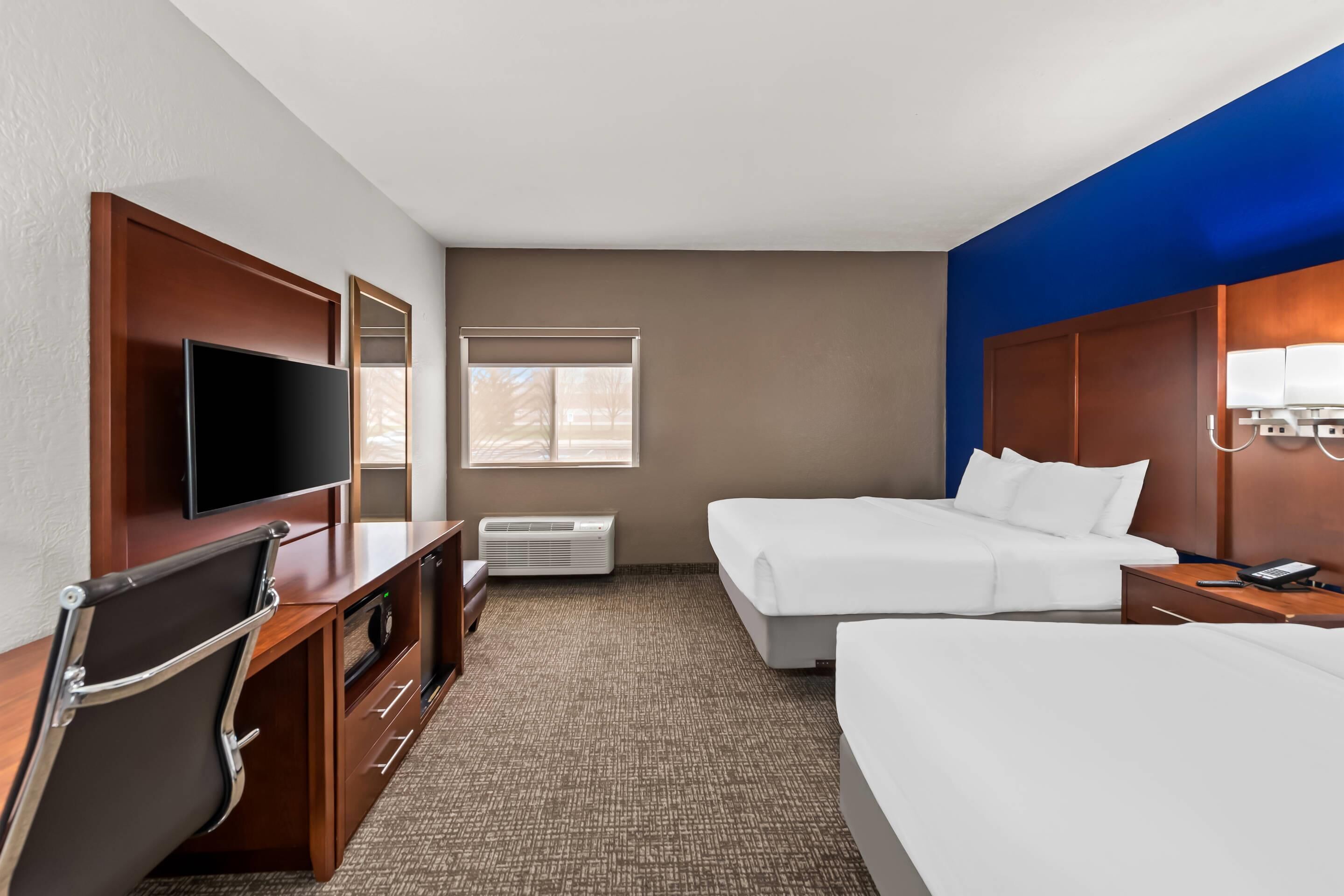 Habitación de hotel con televisión de pantalla plana, escritorio con silla, dos camas, ventana y unidad de aire acondicionado.