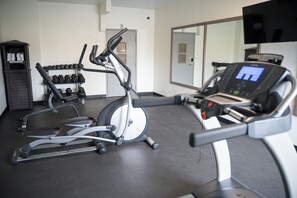 Un gimnasio con máquinas de cardio, mancuernas y una pantalla de televisión.