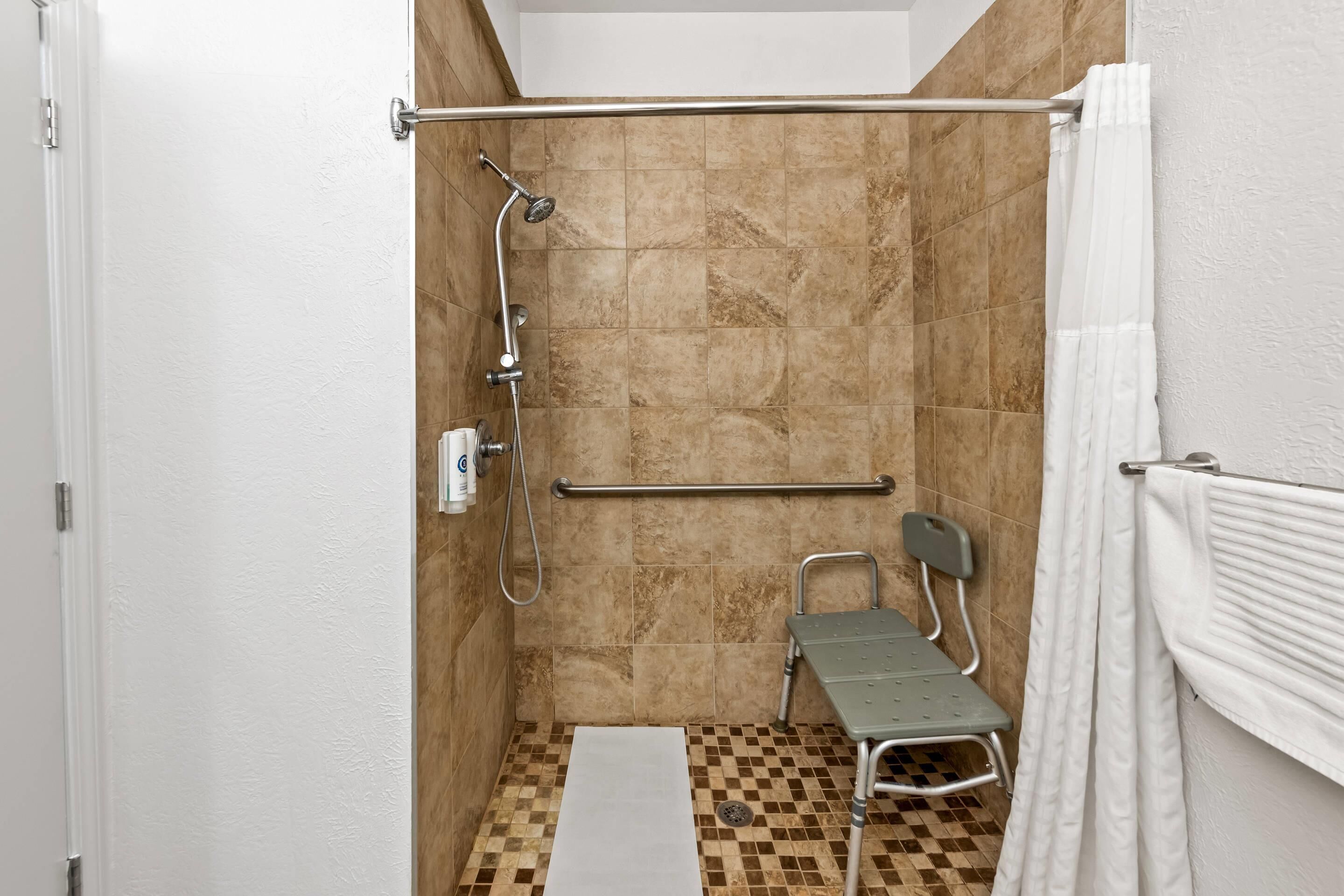 Un área de ducha pequeña y cerrada con ducha, barra de apoyo y un asiento accesible para silla de ruedas.
