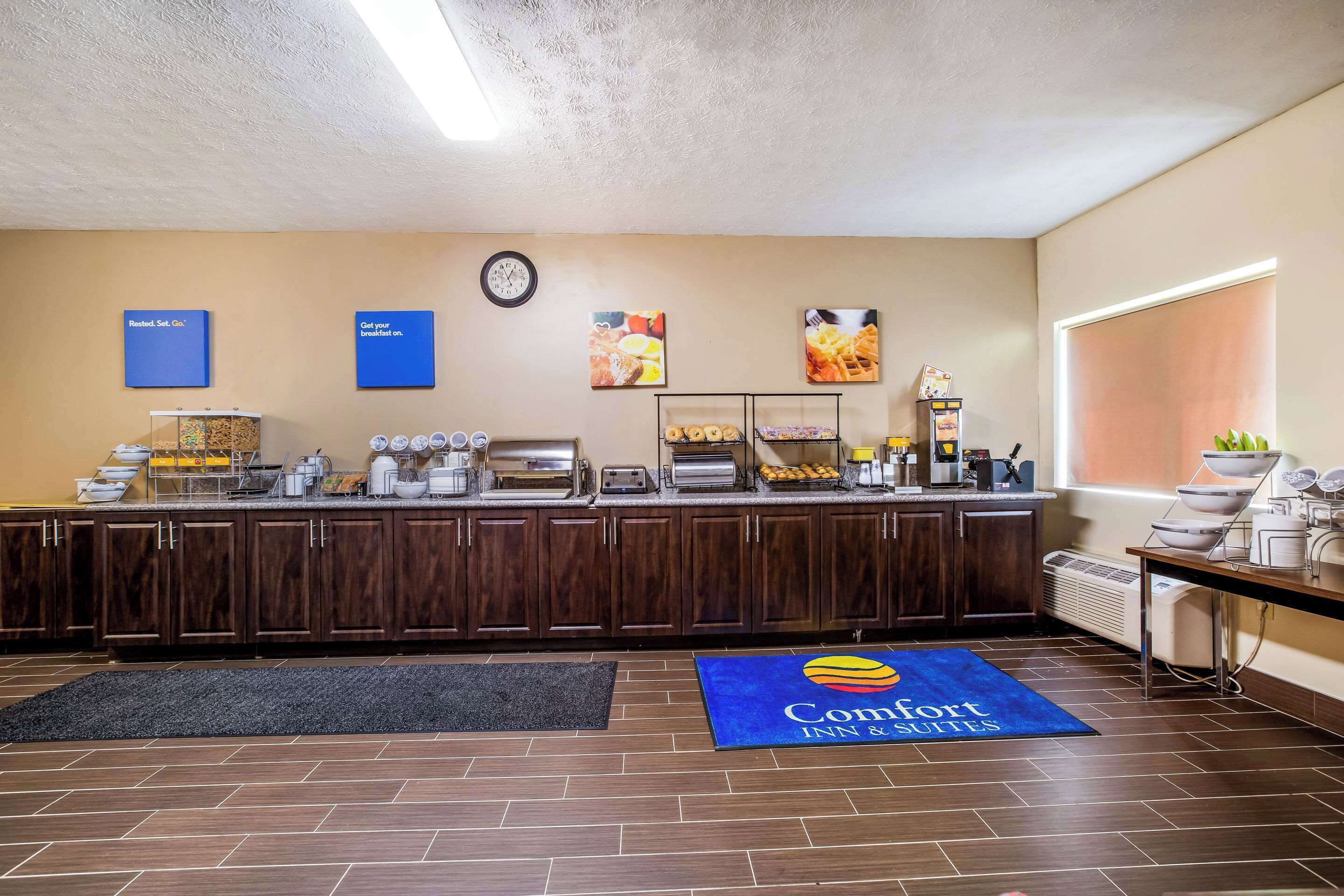 A hotel breakfast area with a buffet setup, a clock, and a blue mat with the hotel logo.
