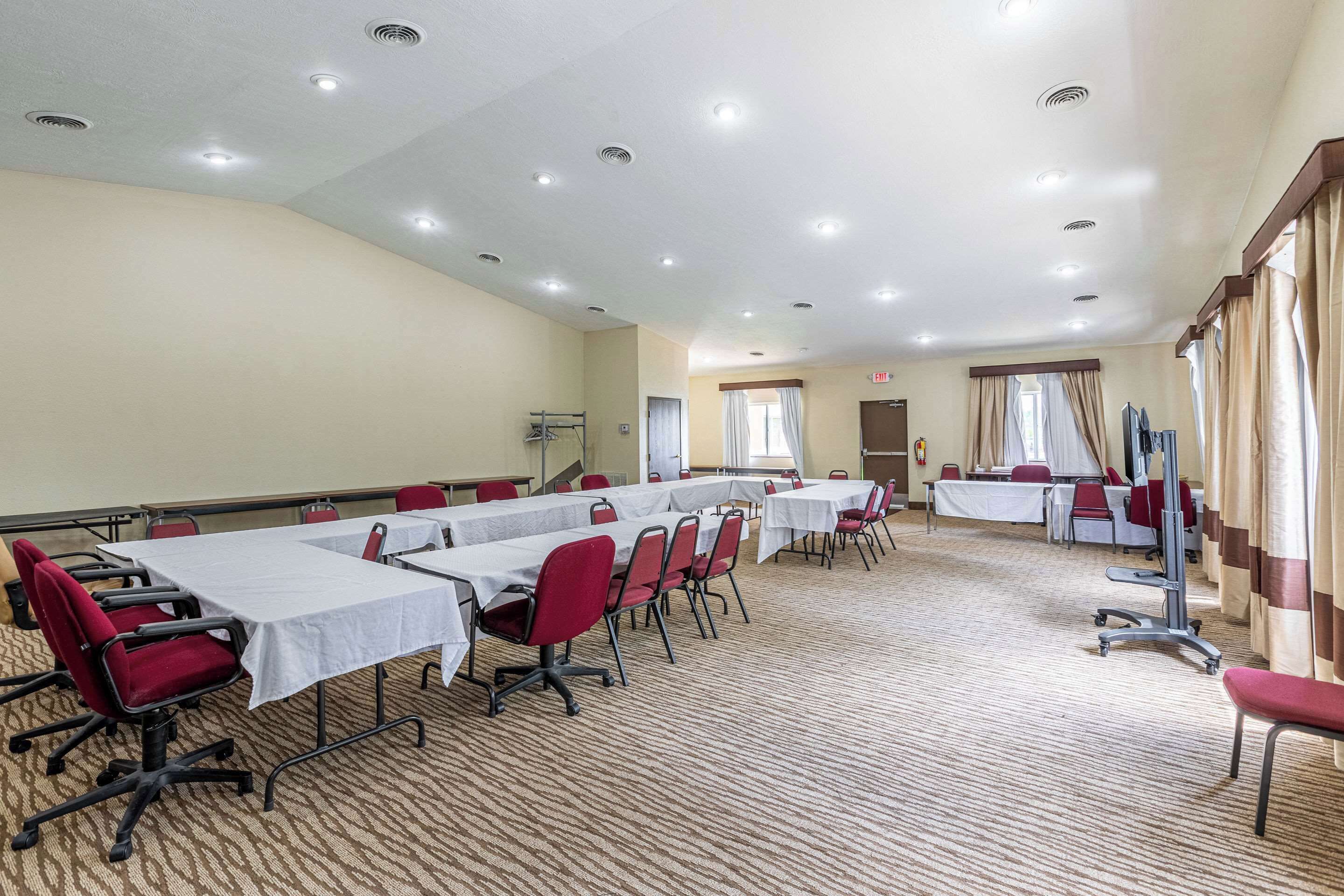 A conference room with multiple tables and chairs, carpeted floor, and ceiling lights.