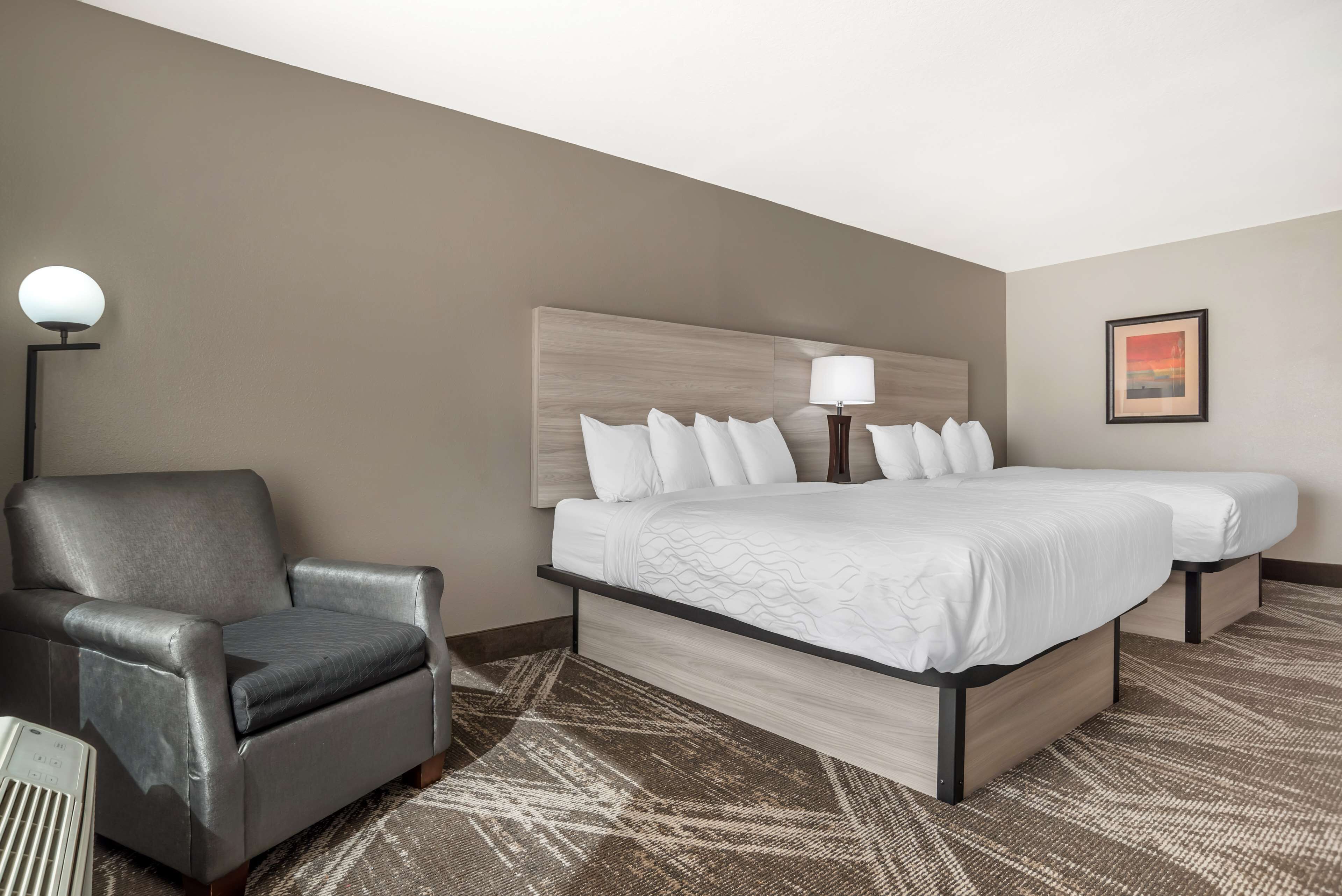 Ein Hotelzimmer mit einem großen Bett, einem Sessel, einer Lampe und einem gerahmten Bild an der Wand.