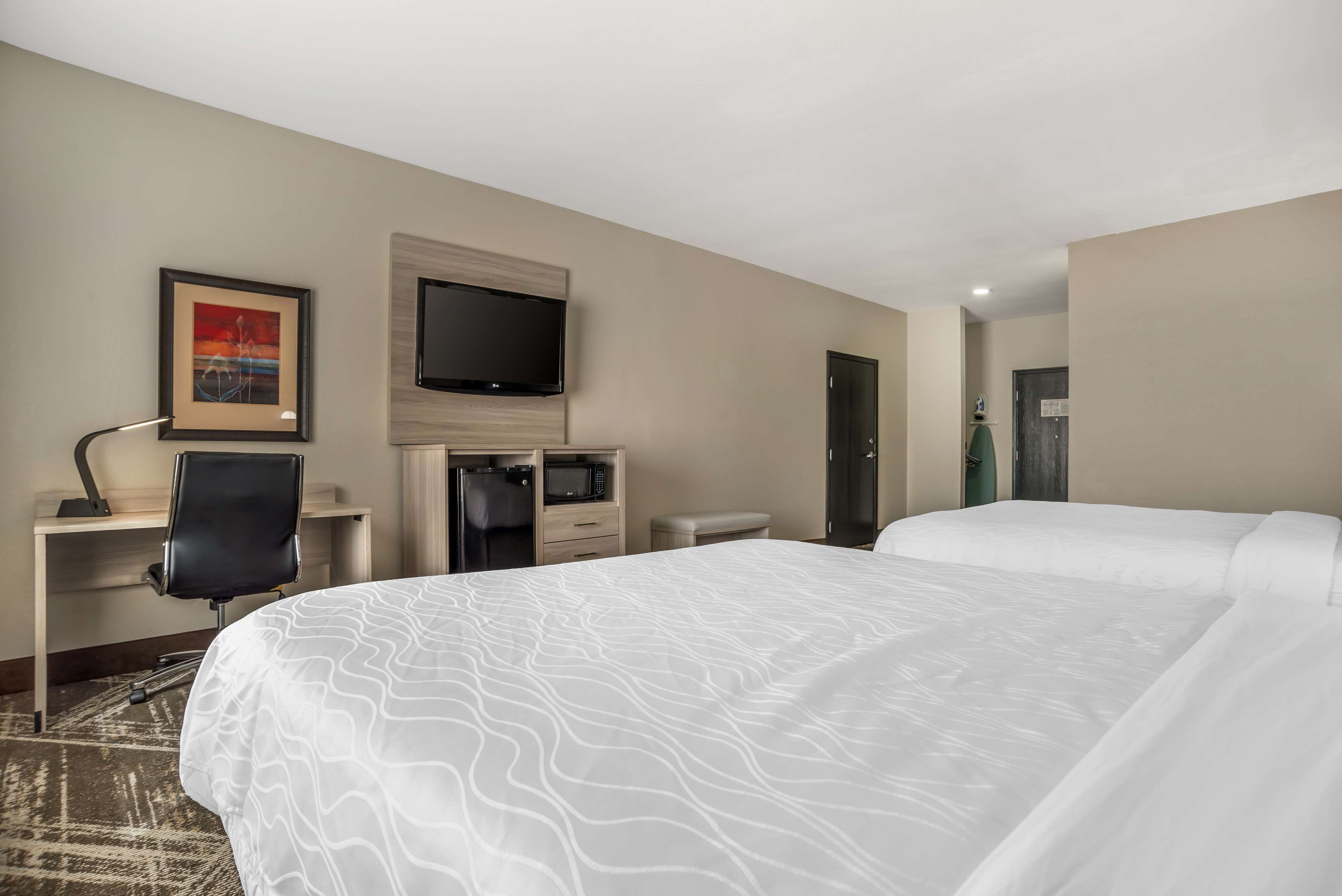 Quarto de hotel com uma cama grande, uma escrivaninha com cadeira, uma televisão de tela plana na parede e um micro-ondas.
