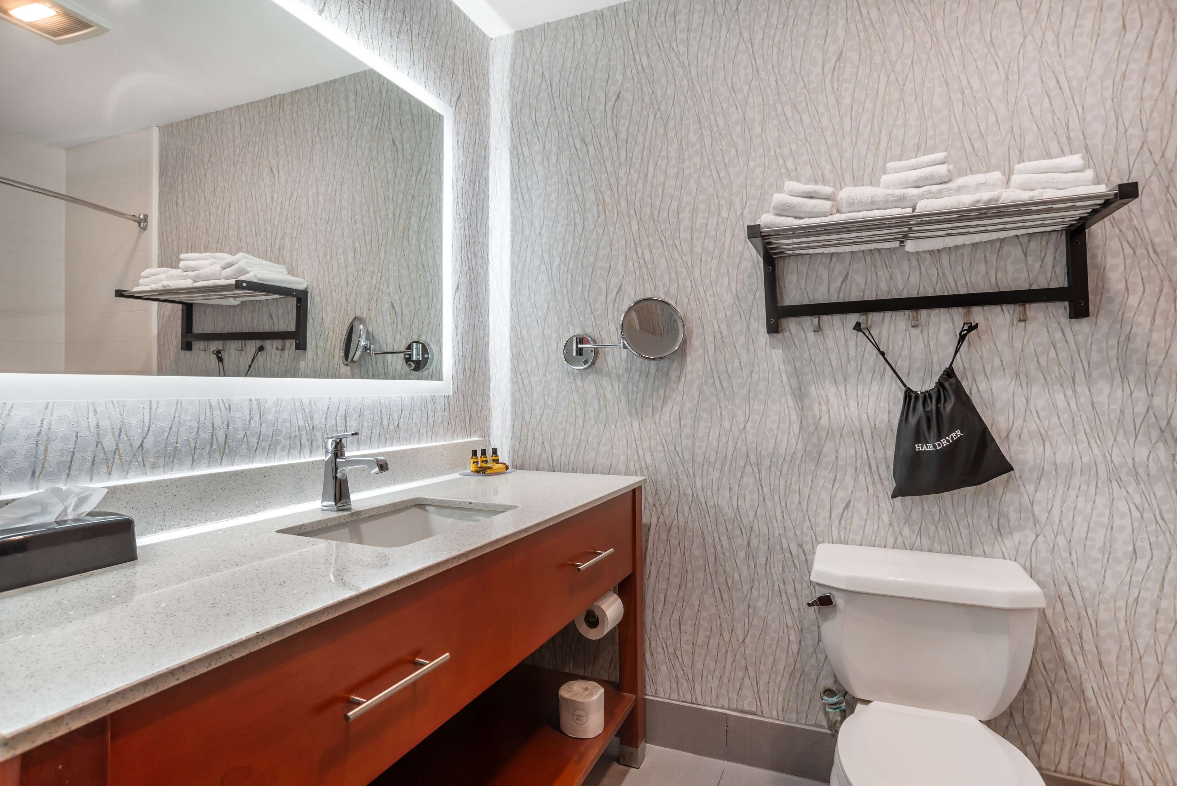 A bathroom with a marble wall, a sink with a mirror, a towel rack, and a toilet.