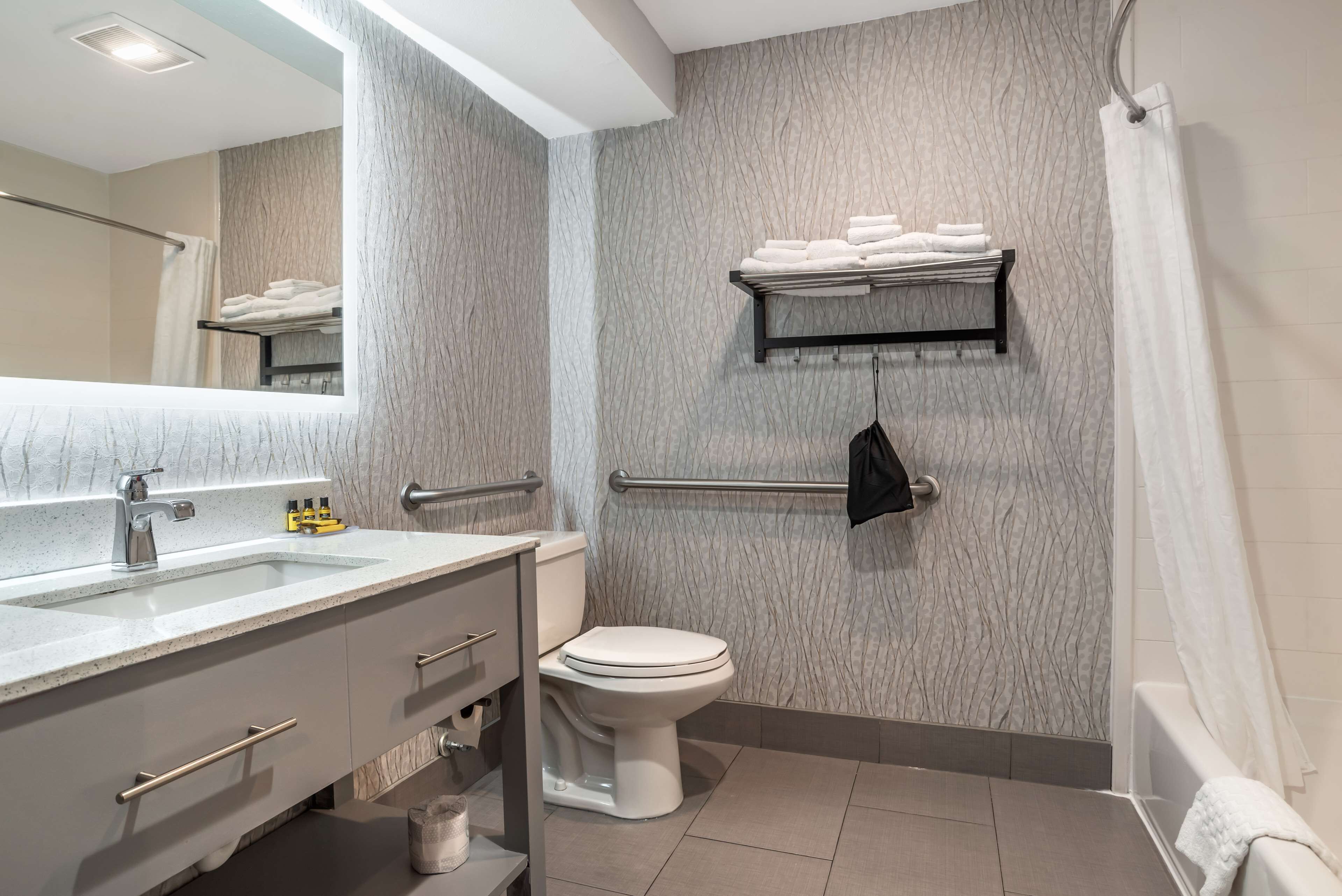 A modern bathroom with a marble backsplash, a white sink with a mirror, a toilet, and a towel rack with folded towels.