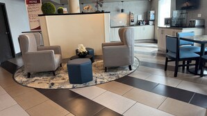 En modern hotellobby med en receptionsdisk, en sittgrupp och ett litet pentry.