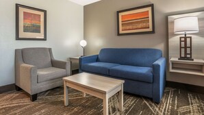 Ett hotellrum med en grå fåtölj, en blå soffa, ett litet träbord och två inramade konstverk på väggarna.