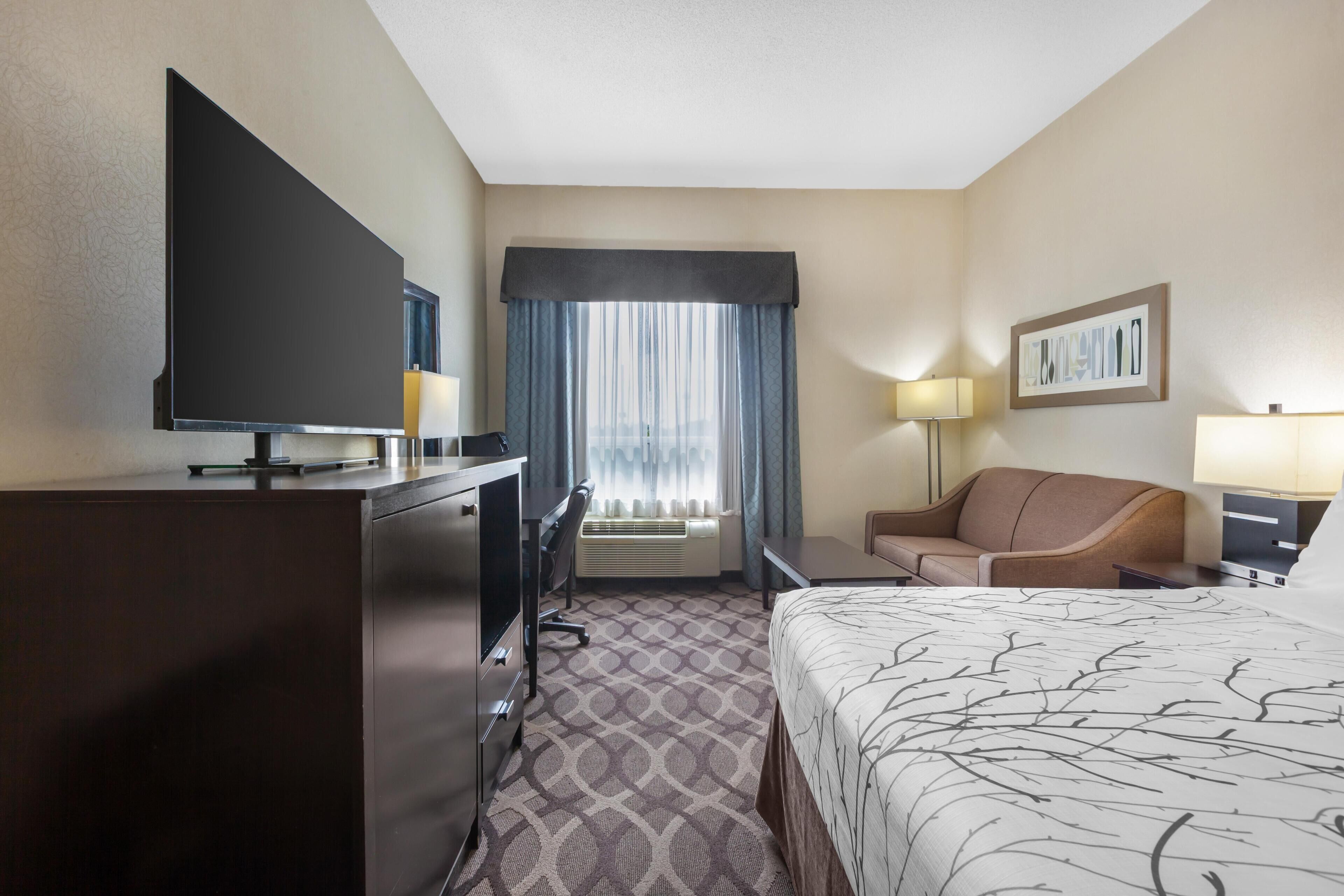 A hotel room with a bed, a desk, a television, a couch, and a window with curtains.