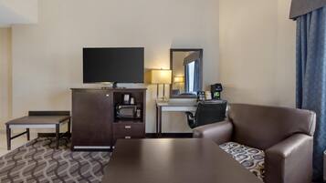 A hotel room with a flat-screen TV, a desk with a lamp, a microwave, a coffee maker, a sofa, and a patterned rug.