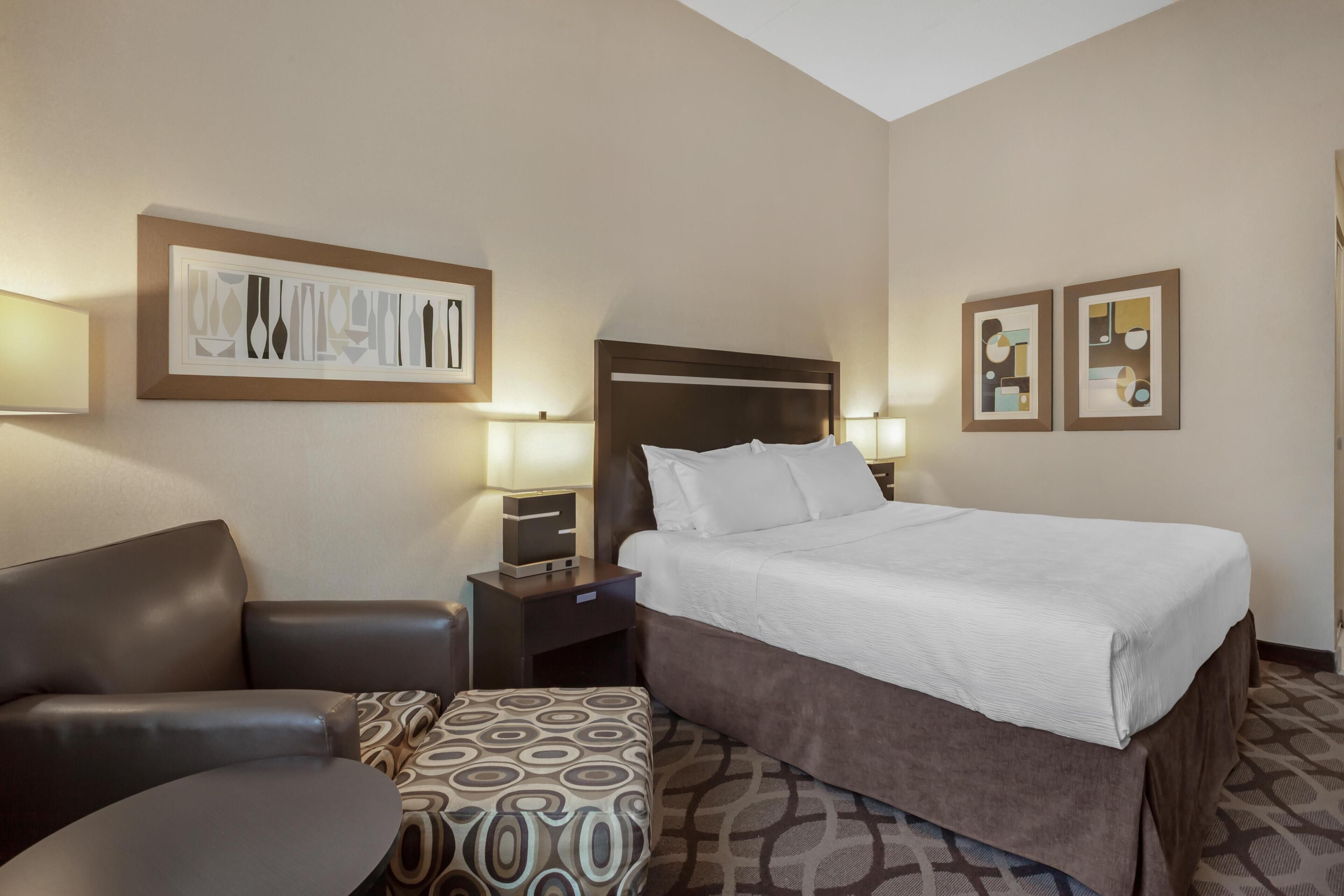 A hotel room with a bed, a desk, a chair, and two wall-mounted lamps.